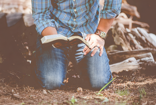 Image of a man on his knees in the dirt holding a bible.