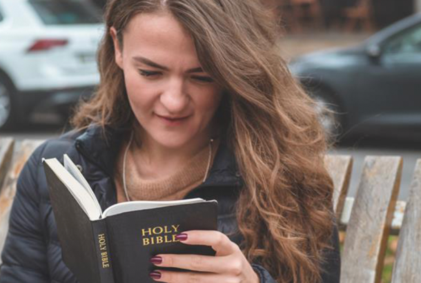 A young woman reading a bible, sitting on a bench