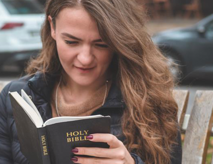 A young woman reading a bible, sitting on a bench