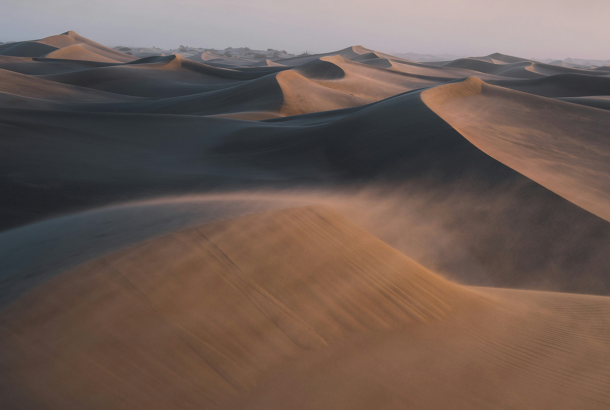Image of a desert with wind blowing over sand dunes.