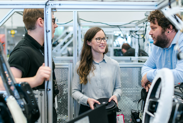 Men and women in a car factory having a conversation.