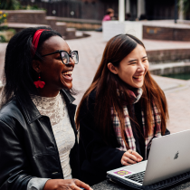 Two women sat outside at a table laughing and reading the Everyday Faith Bible